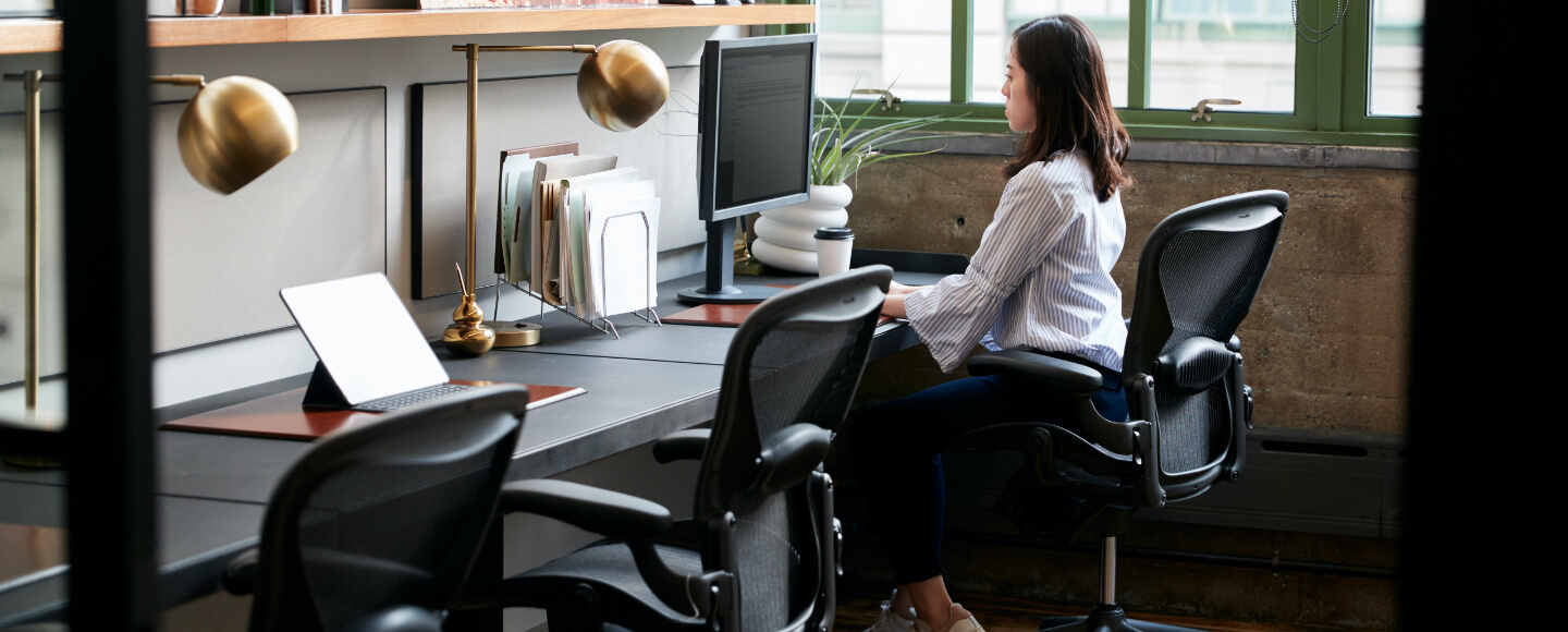 Woman sits at desk in cubicle.