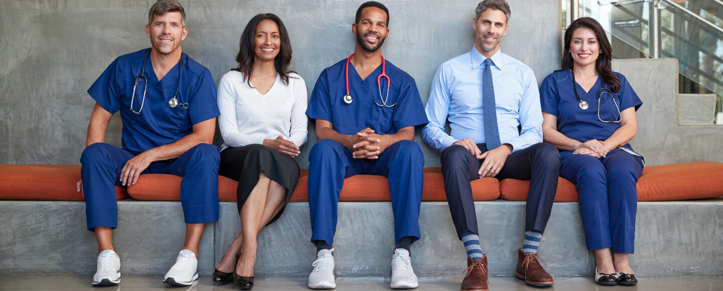 Medical professionals sit in a row on a bench.