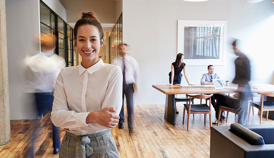 Woman smiles for the camera with busy office behind.