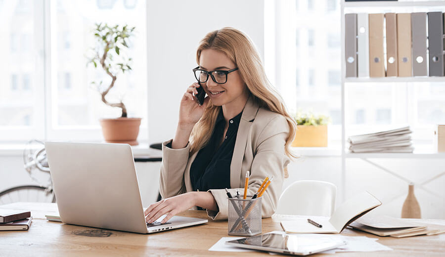 Woman works at her laptop while on the phone.